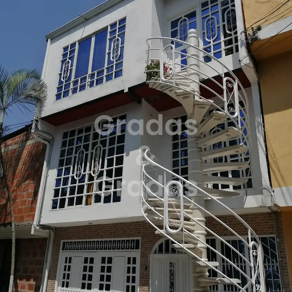 Grada caracol exterior con peldaños claros y pasamanos metálico junto a una vivienda